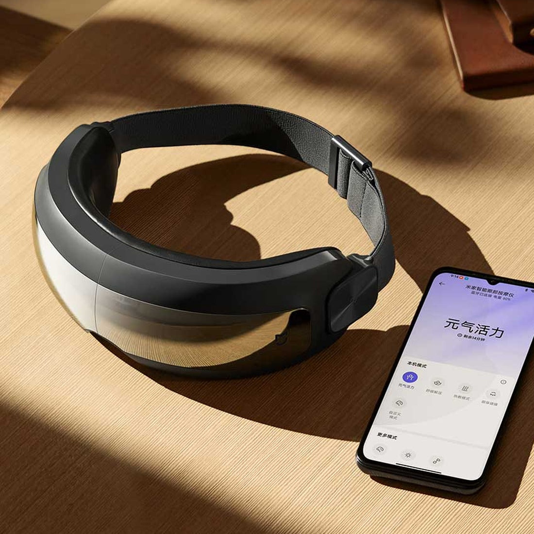 Xiaomi Mijia Smart Eye Massager on a wooden table with app illustration; phone not included